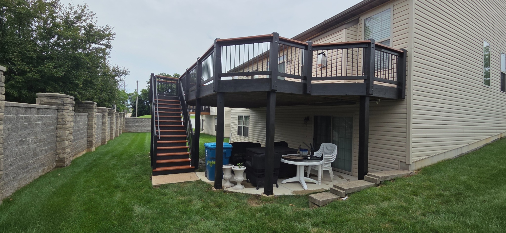 Completed elevated backyard deck with black railings, coordinating stairs, and a covered patio below