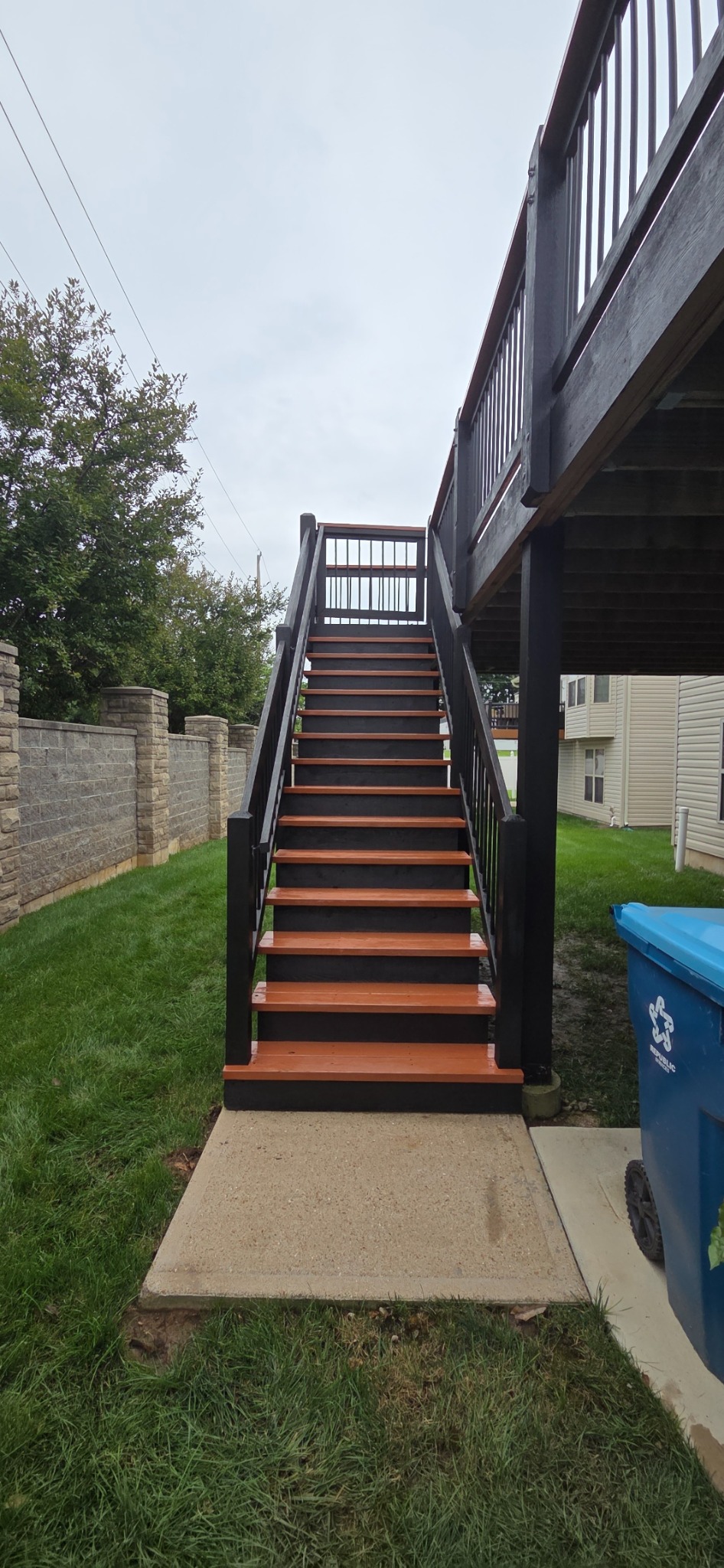 Rebuilt deck staircase with black railings, dark risers, and warm-toned stair treads